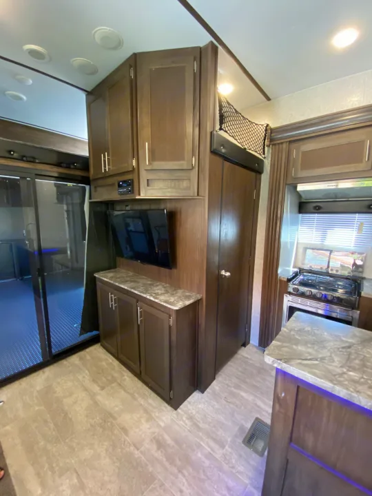 Inside a modern RV rental: well-equipped kitchen with a stove, cozy living area with TV, and stylish dark wood cabinets.. Forest River Xlr Thunrderbolt 2020