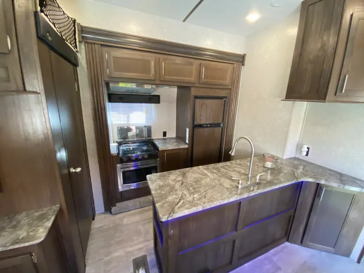 RV rental kitchen interior: modern cabinets, marble counters, stove, microwave, fridge, and sink. Under-cabinet lighting adds ambiance.. Forest River Xlr Thunrderbolt 2020