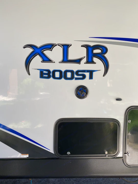 Detailed side of an XLR Boost RV rental, showcasing bold blue branding, an outdoor speaker, and accessible storage compartments.. Forest River Xlr Thunrderbolt 2020
