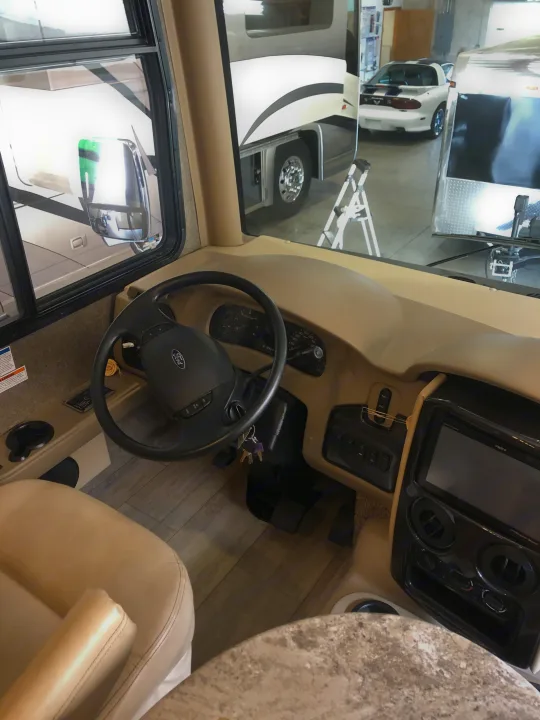 RV rental driver's cockpit view: Ford steering wheel, dashboard, and plush seat. Other vehicles visible outside.. Thor Motor Coach Challenger 2018