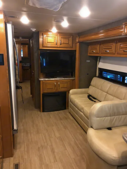 Explore this inviting RV rental: a cream sofa, built-in TV & fireplace, wood cabinets, and an aisle leading to the back.. Thor Motor Coach Challenger 2018