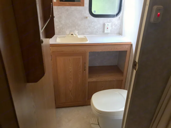 Inside an RV rental bathroom, featuring a clean sink, wood cabinet, window, and toilet. Ready for your travel comfort.. Sunline Solaris/Delivery&Set-up 2002