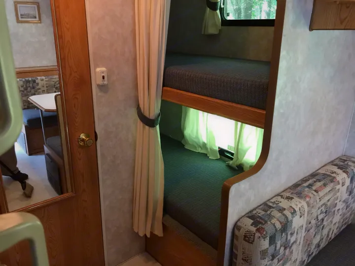 RV rental interior features bunk beds, a dinette, and a sweeping person visible in a mirrored door. Compact travel space.. Sunline Solaris/Delivery&Set-up 2002