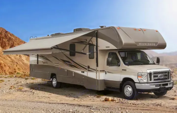 This beige Winnebago motorhome, ideal for an RV rental, is parked in a desert with its awning extended for shade.. Winnebago Winnebago Spirit 2017