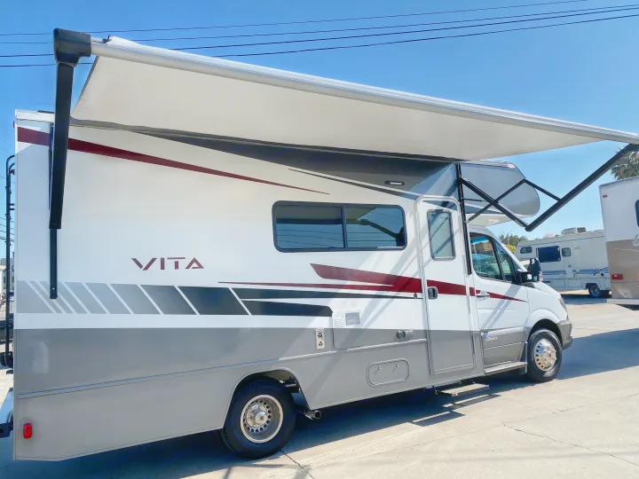 Modern white & grey Class C RV with an extended awning under a clear sky, ready for rv rental.. Winnebago Vita 2020