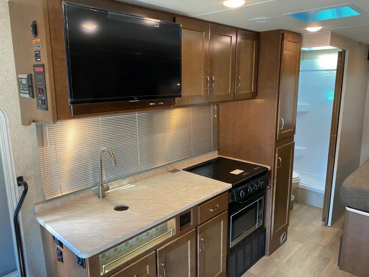 Inside a well-equipped RV rental, showcasing a kitchen with sink, stove, microwave, and TV, leading to a bathroom. Ideal for motorhome travel.. Winnebago Vita 2020