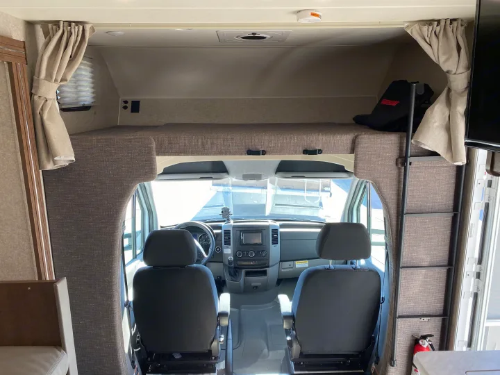 RV rental interior showing the over-cab bunk and front cockpit area with driver and passenger seats.. Winnebago Vita 2020