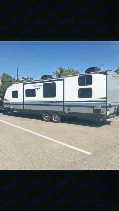 A large white and gray Surveyor travel trailer, available for rv rental, parked on asphalt on a sunny day.. Forest River Surveyor bunkhouse 2018
