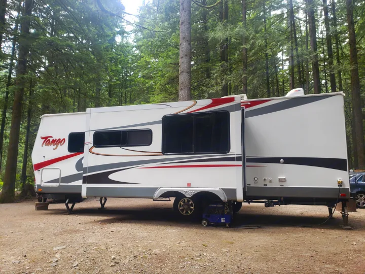 Tango RV rental parked at a forest campsite with a generator. This white travel trailer is perfect for outdoor adventures.. Pacific Coachworks Tango 2010