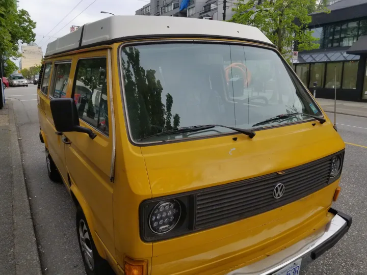 This bright yellow Volkswagen camper van, possibly an RV rental, is parked on a city street, ready for adventure.. Volkswagen Westfalia 1982