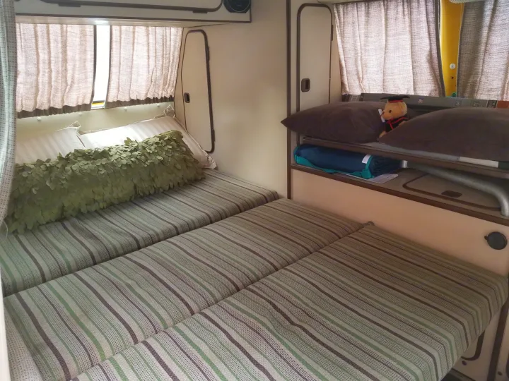 Cozy RV rental interior featuring striped beds, soft pillows, and curtains for comfortable travel.. Volkswagen Westfalia 1982