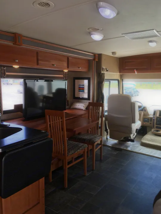 Spacious RV rental interior featuring a kitchen, dining area with wooden table & chairs, & front cockpit view. Ideal for travel.. Winnebago Itasca Sunova 2014