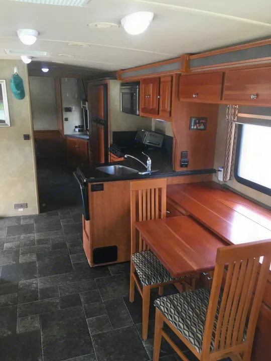 Spacious RV rental kitchen & dining area features wood cabinets, black counters, a sink, & tiled floors.. Winnebago Itasca Sunova 2014