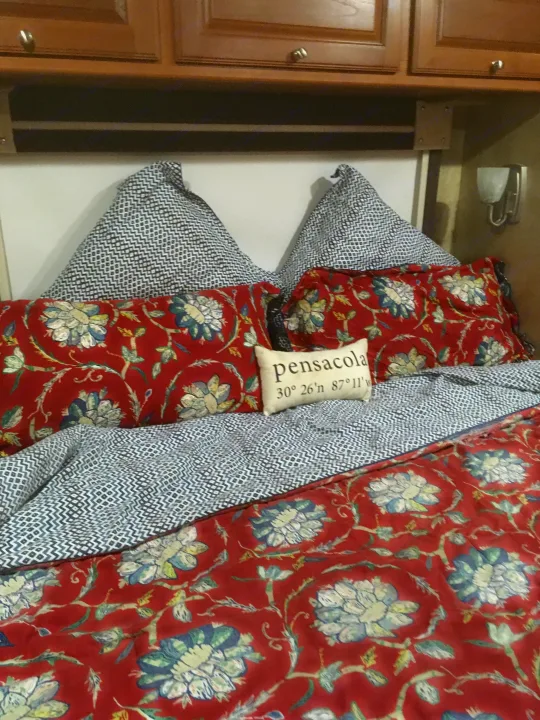 Comfortable RV rental bedroom featuring vibrant red floral and geometric patterned bedding, topped with a 'Pensacola' coordinates pillow.. Winnebago Itasca Sunova 2014