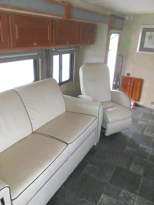 RV rental interior with light-colored sofa and recliner featuring black piping, wood cabinets, and dark tiled floor.. Winnebago Itasca Sunova 2014