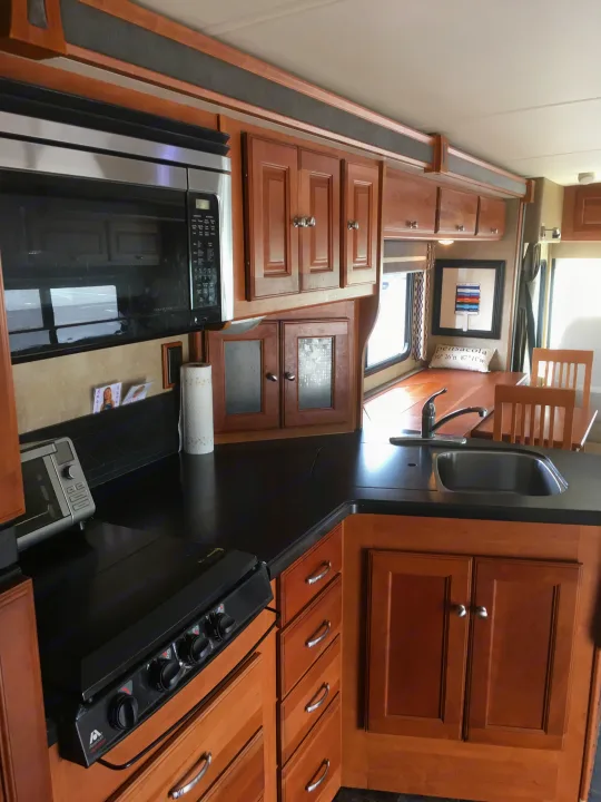 RV rental featuring a modern kitchen with a microwave, stove, sink, and bright dining area.. Winnebago Itasca Sunova 2014