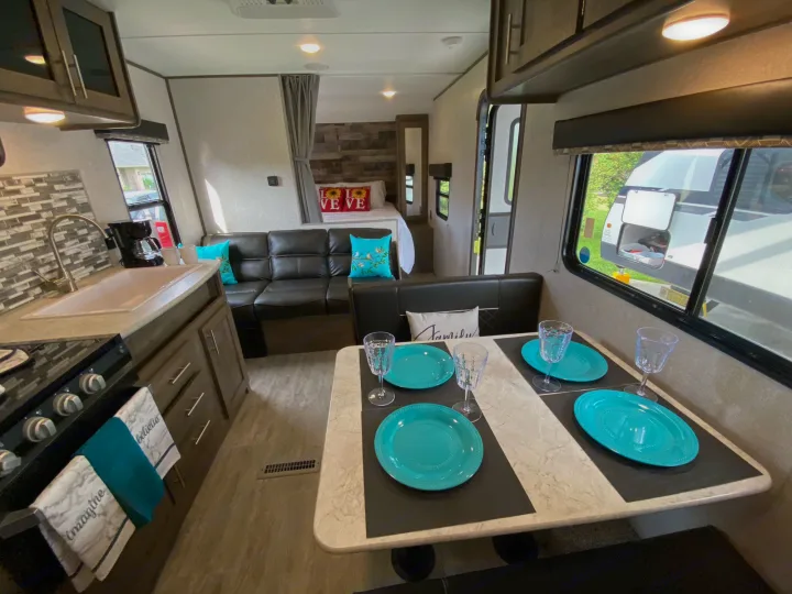 Inside a bright rv rental: modern kitchen, cozy dining area set with turquoise plates, comfortable sofa, and a welcoming bedroom.. Dutchmen Aspen Trail 2021
