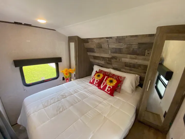 Relaxing RV rental bedroom featuring a comfy bed with "LOVE" pillows, wood accent wall, and bright window.. Dutchmen Aspen Trail 2021