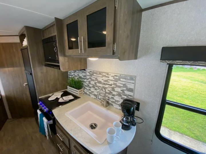 Compact and modern RV rental kitchen with a light pink sink, stove, microwave, and coffee maker. Ready for your adventure.. Dutchmen Aspen Trail 2021