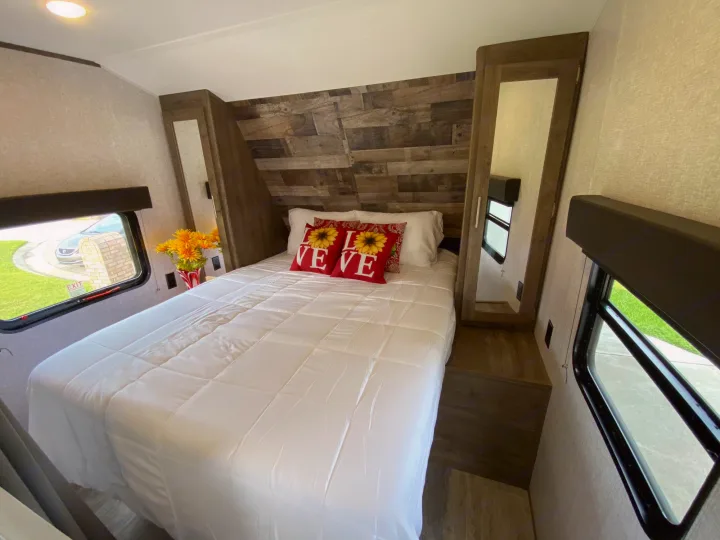 RV rental bedroom with bed, sunflower LOVE pillows, wood paneling, and windows. Ready for your cozy trip.. Dutchmen Aspen Trail 2021