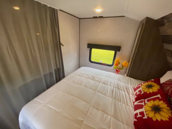 Cozy RV rental bedroom with comfortable bed, sunflower pillows, bright window view, and neutral decor for your travels.. Dutchmen Aspen Trail 2021