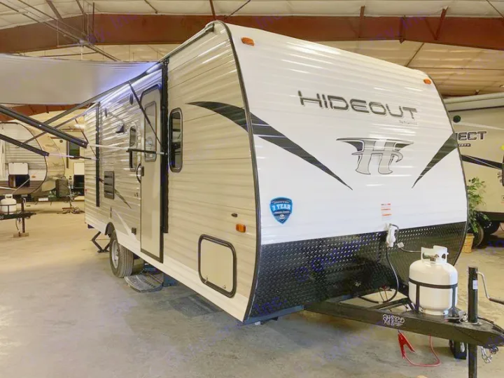 New white and beige Hideout travel trailer, great for your next rv rental adventure. Awning extended, propane tank visible.. Keystone Hideout 2019