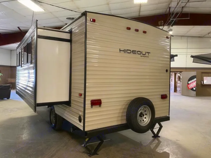 Beige travel trailer, 'Hideout' RV, with extended side slide-out and rear spare tire, ready for rv rental.. Keystone Hideout 2019