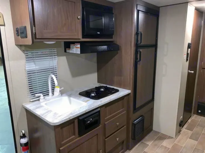 Explore our RV rental's functional kitchen: sink, two-burner stovetop, microwave, fridge, and cabinets for your travels.. Keystone Hideout 2019