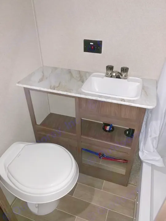 Compact RV rental bathroom features a white toilet, sink vanity with open shelving, and a nearby shower.. Keystone Hideout 2019