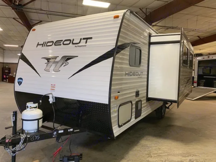 White and black Hideout by Keystone travel trailer, ideal for rv rental, featuring a large opened slide-out, parked indoors.. Keystone Hideout 2019