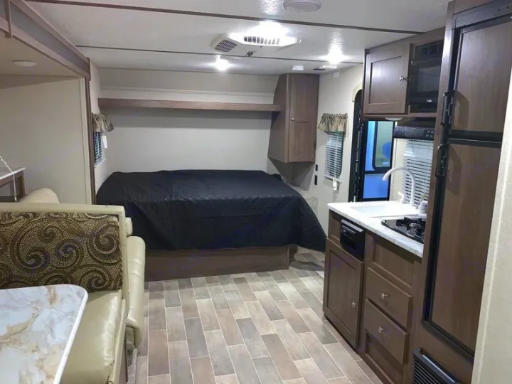 Inside an RV rental: a full bed, compact kitchen with sink/stove, and a dinette for comfort.. Keystone Hideout 2019