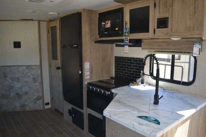 Spacious RV rental interior featuring a modern kitchen with black appliances, white marble-look counters, and wood flooring.. Forest River Other 2020
