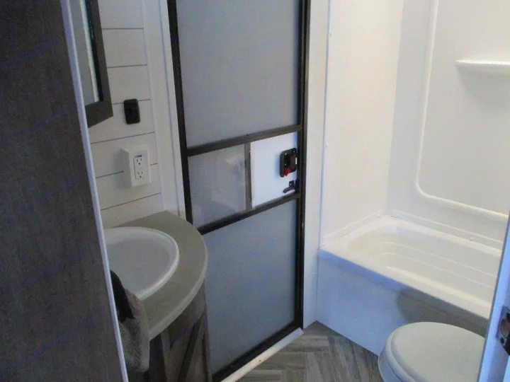 Bright rv rental bathroom. Left shows sink, mirror, and shiplap wall. Right reveals compact shower/tub and toilet behind frosted door.. Forest River Evo 2021