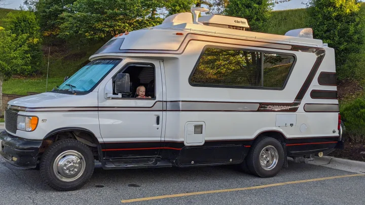 A child smiles from a white Chinook rv rental. This spacious campervan with roof AC is ready for family adventures.. Chinook Concourse 2001
