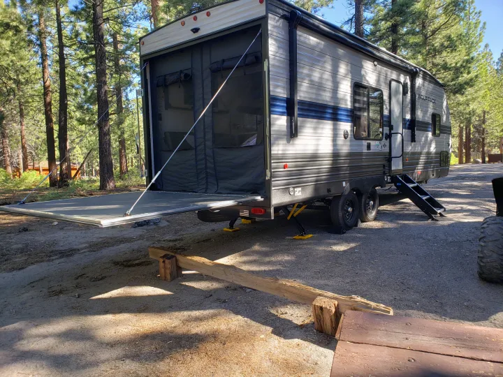 An RV rental toy hauler with its back patio ramp down, ideal for forest camping adventures.. Forest River Cherokee Wolf Pack 2021