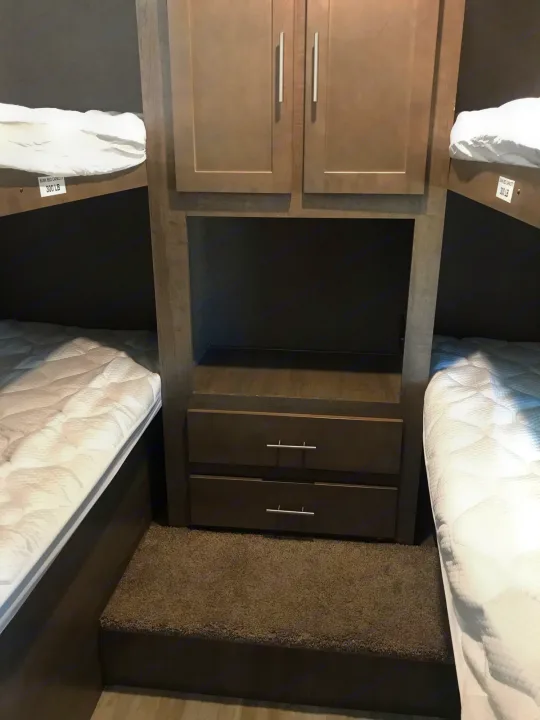 View inside an RV rental showing cozy bunk beds on each side, with a central storage unit, shelves, and drawers.. Forest River Surveyor bunkhouse 2018
