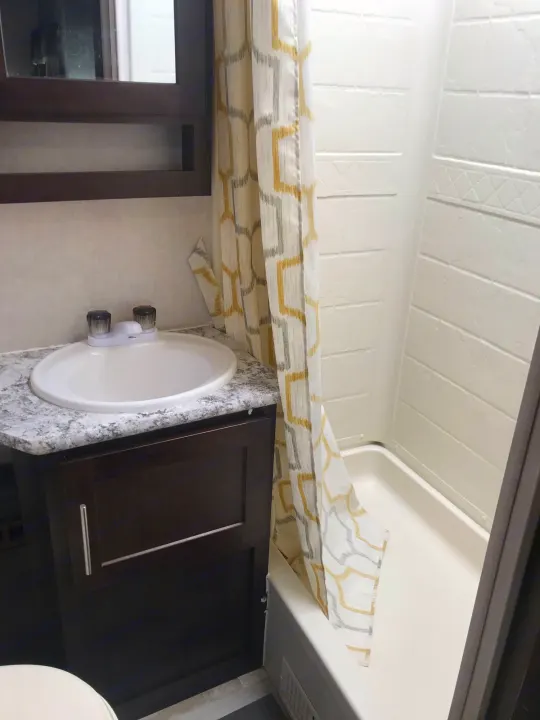 RV rental bathroom: white sink, dark vanity, and shower with a yellow-grey patterned curtain.. Forest River Surveyor bunkhouse 2018