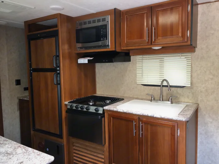 RV rental kitchen featuring a refrigerator, microwave, gas range with oven, sink, and warm wood cabinetry.. Prime Time Tracer 2017