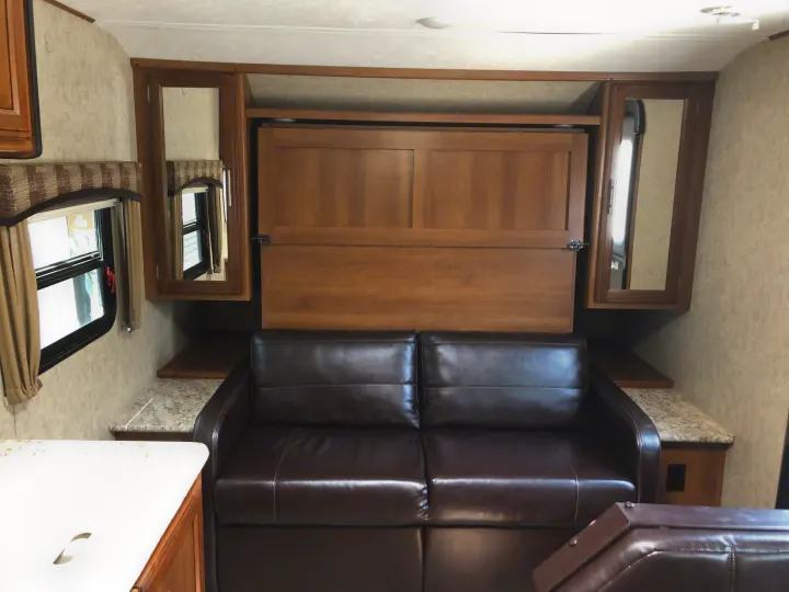 This RV rental interior features a dark leather sofa, a space-saving murphy bed unit, and compact cabinetry.. Prime Time Tracer 2017