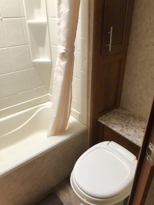 Compact rv rental bathroom featuring a white tub/shower with curtain, toilet, and storage cabinet. Functional space.. Prime Time Tracer 2017