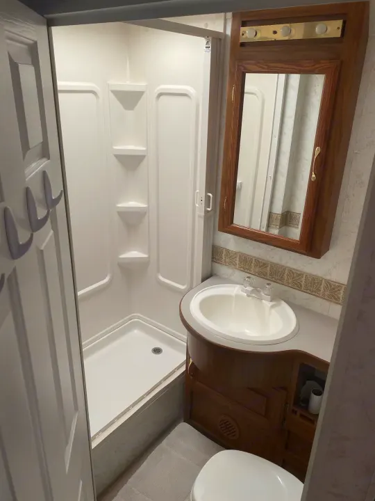 Explore this RV rental's compact bathroom featuring a shower stall, wood-framed mirror, sink, and toilet for comfortable travel.. Dutchmen Four Winds 2003