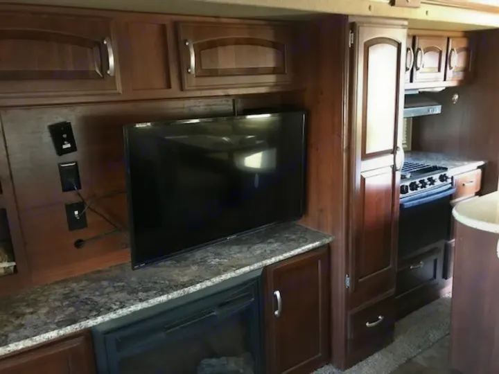 RV rental interior: A dark wood living area with mounted TV, fireplace, and integrated kitchen with stove. Compact & functional.. Keystone 316-UL 2014