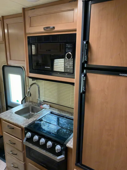 RV rental interior: A well-equipped compact kitchen featuring a microwave, refrigerator, sink, stove/oven, and storage.. Thor Chateau 2019