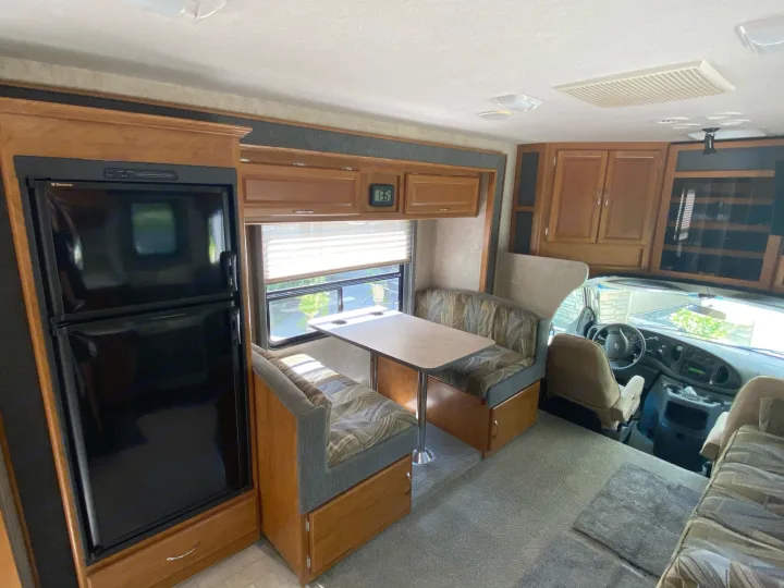 This rv rental interior features a fridge, dinette, and driver's area, offering a home-like space for your travels.. Fleetwood Jamboree 2005