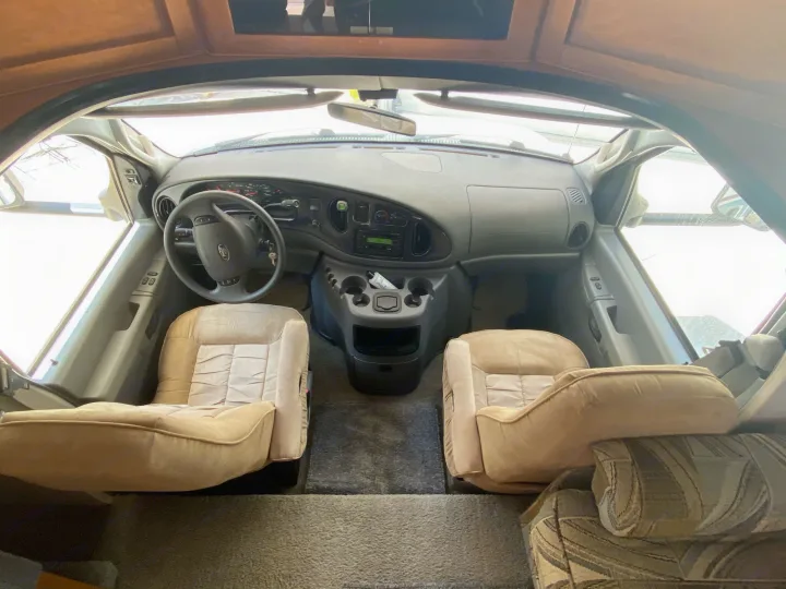 Inside an RV rental's front cabin, showing beige seats, Ford steering wheel, and dashboard. Ready for the road.. Fleetwood Jamboree 2005