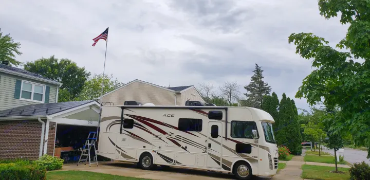 Large white Thor ACE RV rental parked in driveway with flag pole on roof, under a cloudy sky.. Thor Motor Coach 30.3 2019