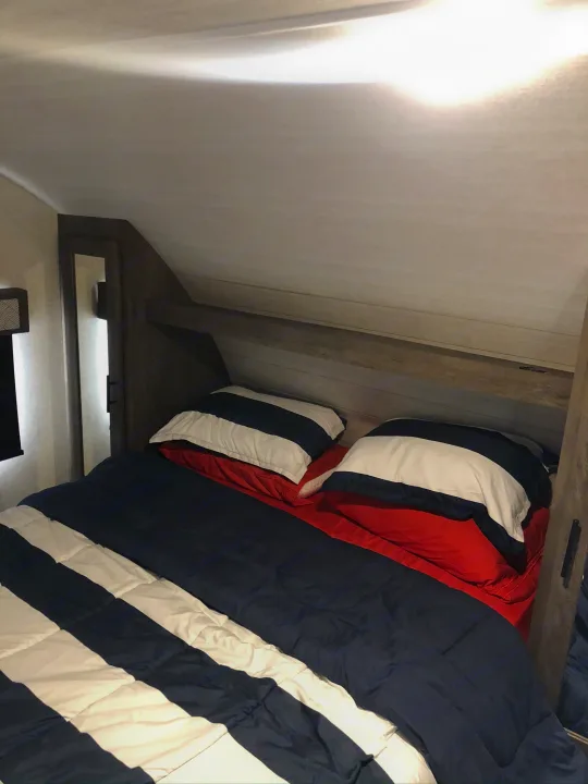 Cozy RV rental bedroom: blue & white striped comforter, red sheets, and built-in storage. Compact and comfortable.. Forest River Wildwood X-Lite 2020