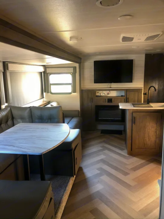 Modern RV rental interior: spacious dining area, cozy living space with a TV & fireplace, and stylish herringbone floor.. Forest River Wildwood X-Lite 2020