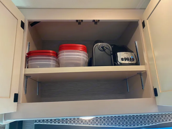 Inside an RV rental kitchen cabinet: Organized plastic food containers, a coffee maker, and an Oster blender for convenience.. Thor A.C.E 2020