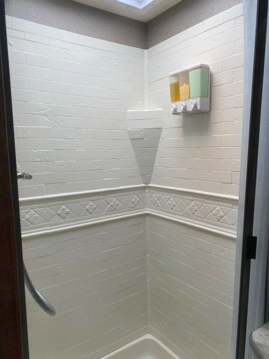 Clean RV rental shower featuring white faux brick walls, a corner shelf, and a wall-mounted triple soap dispenser.. Thor A.C.E 2020